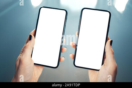 Woman hands holding side by side two smart phones. Comparing, analyzing or matching two products or services - concept. Clean and blurred modern backg Stock Photo