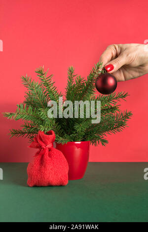 Womans hand decorates small red Christmas tree with gift bag. Close up. Xmas card. Holiday winter time. Stock Photo