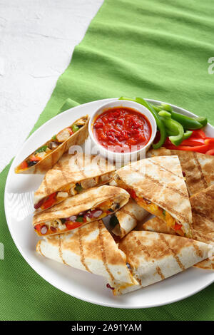 mexican chicken quesadillas with vegetables, shredded cheddar cheese, olives and mushrooms on a white plate with tomato salsa, vertical view from abov Stock Photo