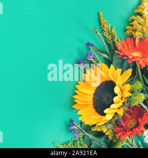 Corner border of different fresh bright colorful summer flowers lying on trendy mint background. Flat lay style. Copy space. Stock Photo