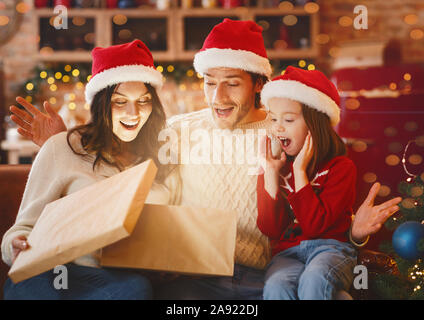 Surprised family opening Christmas gifts together in festive kitchen Stock Photo