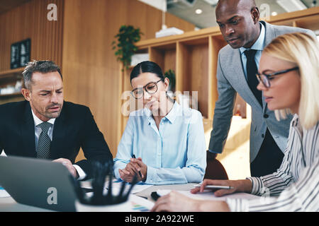 Focused group of diverse businesspeople going over paperwork and working on a laptop together during an office meeting Stock Photo