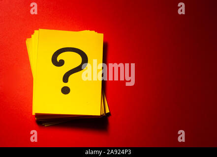 A question mark on a yellow paper card and on a dark red background. Stock Photo