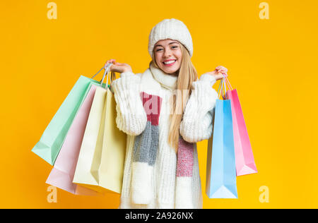 Emotional blonde woman in woollen hat holding shopping bags Stock Photo