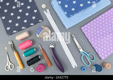Overhead flat lay with various different sewing tools like fabric, thread, zipper, scissors, spool, thread seperator, pincushion or rotary cutter on g Stock Photo