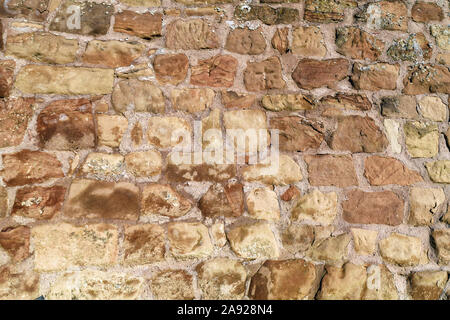 Background with uneven old historic wall with brown irregular different sized and shaped sandstone stones in gray concrete Stock Photo