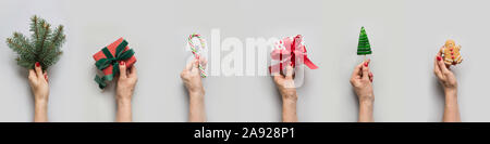 Female hands holding different gifts, Christmas tree, lollipop, gingerbread on grey. Xmas greeting card. Isolated. Xmas banner for design. Boxing day. Stock Photo