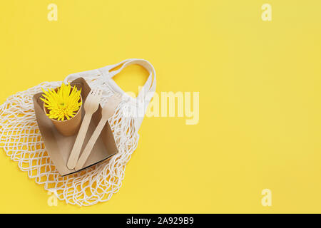Eco-friendly disposable utensils and flower from above Mesh textile bag on yellow background. Zero waste shopping. Ecological concept. Stock Photo