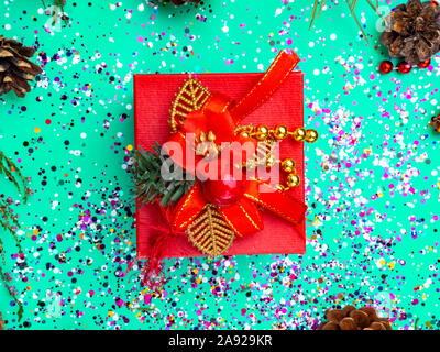 Red gift box with red decoration on turquoise background with colorful glitter, cones. Holiday concept. Topo view Stock Photo