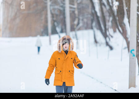 man in yellow winter coat with hood walking by snowed park Stock Photo
