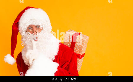 Santa holding finger near mouth and hiding Christmas gift Stock Photo