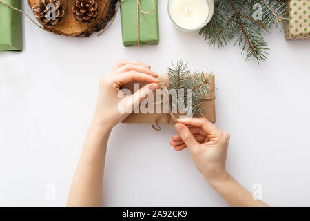 Female hands hold a box with a Christmas gift on white table with Christmas decorations. Christmas, Xmas, winter, new year, zero waste concept. Flat Stock Photo