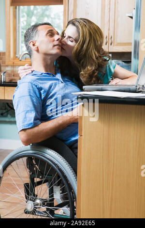 Mid adult woman kissing a mid adult man sitting in a wheelchair Stock Photo