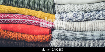 Pile of knitted woolen sweaters autumn colors. Clothes with different knitting patterns folded in stack. Warm cozy winter fall knitwear concept. Stock Photo