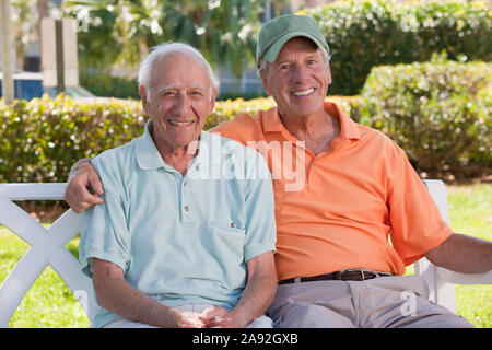 Portrait of two senior men sitting on a park bench and smiling Stock Photo