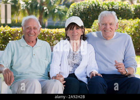 Three senior friends sitting on a park bench and smiling Stock Photo