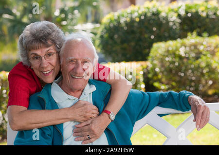 Portrait of a senior woman hugging her husband from behind in a park Stock Photo