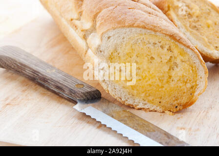 Sliced toasted garlic baguette bread served on a wooden cutting board and an old knife laying off to the side. Stock Photo