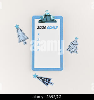 Goals 2020 on clipboard with wooden Christmas trees on white. Holiday decorations and clipboard with wish list on white background, flat lay Stock Photo