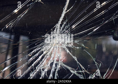 Cracks and glass shards radiate from the point of impact in a window that has been hit by an object Stock Photo