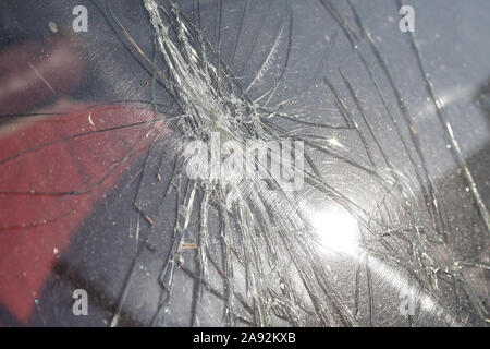 Cracks and glass shards radiate from the point of impact in a window that has been hit by an object Stock Photo