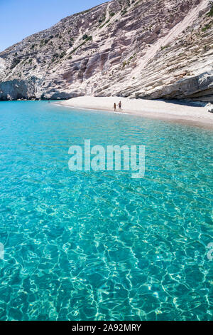 Tourists walking on the beach along the clear, turquoise water of Galazia Nera Bay; Polyaigos Island, Cyclades, Greece
