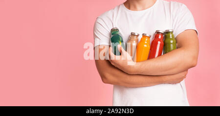 Man holding set of colorful detox drinks in glass bottles on pink Stock Photo
