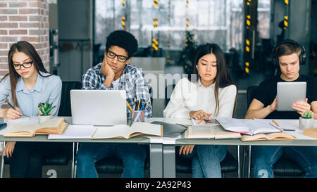 Diverse students studying in university library with gadgets Stock Photo