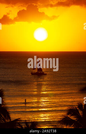 Golden sunset off Waikiki Beach with a silhouetted sailboat in the water; Honolulu, Oahu, Hawaii, United States of America Stock Photo