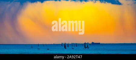 Clouds glowing a bright yellow at sunset off Waikiki Beach with a silhouetted sailboats in the water; Honolulu, Oahu, Hawaii, United States of America Stock Photo