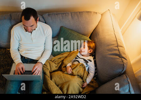 Father using laptop in living room while daughter sleeping next to him Stock Photo