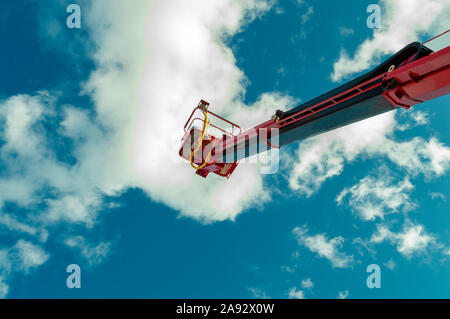 High-altitude hydraulic tower based on a truck on a background of blue sky and white clouds. View from the bottom up. Stock Photo