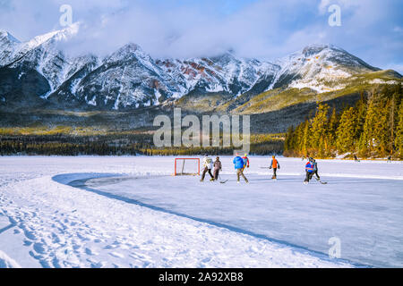 Frozen Pyramid Lake with kids playing hockey on a cleared ice rink in winter, Jasper National Park; Alberta, Canada Stock Photo