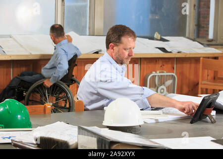 Two project engineers, one with a Spinal Cord Injury in a wheelchair, working at office Stock Photo