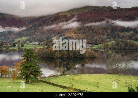 Mist and low cloud hanging over Grasmere island in the middle of Grasmere lake on a rainy autumnal day Stock Photo