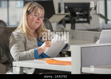 Young woman with Down Syndrome doing paperwork in an office Stock Photo