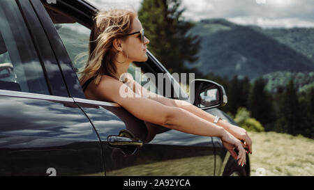 Happy woman travels by car in the mountains. Summer vacation concept. Woman out the window enjoying mountain view Stock Photo