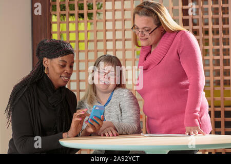 Three women in an office reading text messages, one with Down Syndrome Stock Photo