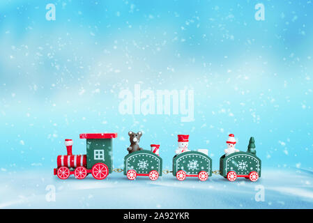Cute train in the snow. Christmas; New Year background. Wooden toy with a bear and two snowshoes in wagons. Blue background. Stock Photo