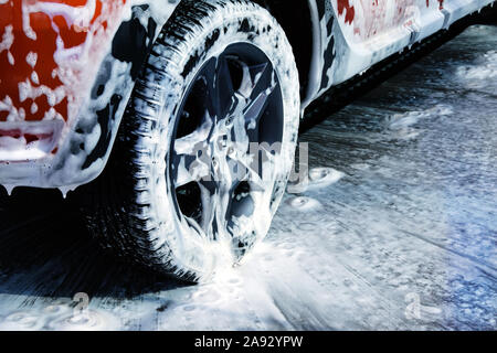 Car wheel close up. Car is cleaning with soap suds at self service car wash. White lather on auto. Stock Photo