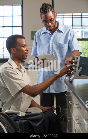 Two students who had Spinal Meningitis collecting data on tablet from oscilloscope in laboratory Stock Photo