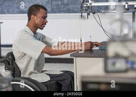 Student with Spinal Meningitis in wheelchair studying acceleration on a frictionless table in laboratory Stock Photo