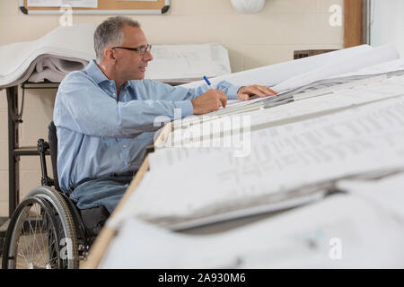 Project engineer with a Spinal Cord Injury in a wheelchair working on drawings Stock Photo