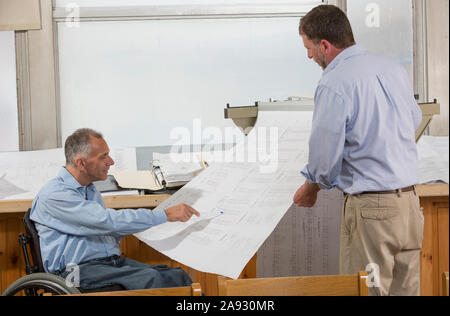 Two project engineers using a hanging rack for job site plans, one in a wheelchair with a Spinal Cord Injury Stock Photo