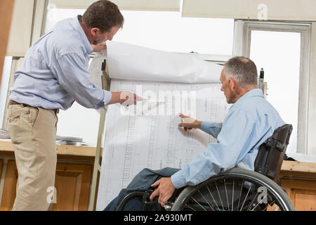 Two project engineers using a hanging rack for job site plans, one in a wheelchair with a Spinal Cord Injury Stock Photo