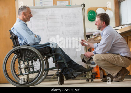 Two project engineers using a hanging rack for job site plans, one in a wheelchair with a Spinal Cord Injury Stock Photo