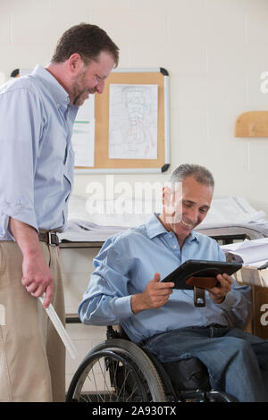 Two project engineers using their tablet to check job site plans, one in a wheelchair with a Spinal Cord Injury Stock Photo
