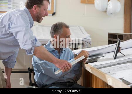 Two project engineers using their tablets to check job site plans, one in a wheelchair with a Spinal Cord Injury Stock Photo