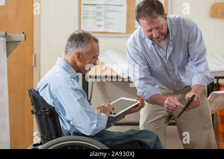 Two project engineers using their tablets to check job site plans, one in a wheelchair with a Spinal Cord Injury Stock Photo