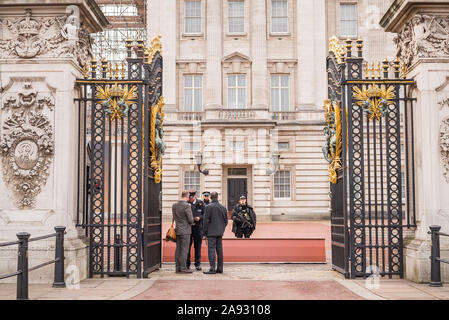 Looking through open front gates of Buckingham Palace, central London, UK. Armed police on guard checking security of visitors. Guarding royal family. Stock Photo